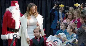  ?? AP/ANDREW HARNIK ?? First lady Melania Trump often wears her overcoat draped over her shoulders, as she did in this appearance with Santa Claus at the Children’s National Medical Center in Washington.