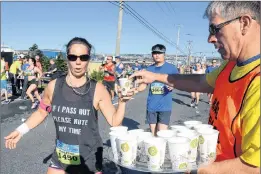  ?? KEITH GOSSE/THE TELEGRAM ?? New RNC police chief Joe Boland passes out water to runners including Colette Decker in the 90th Tely 10 road race Sunday morning.