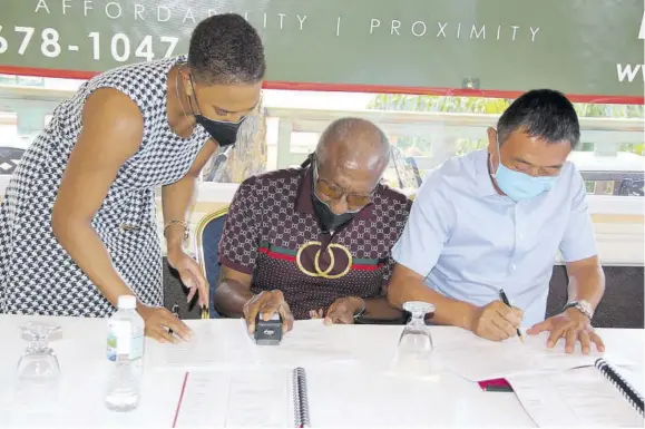  ?? ?? Carl Erskine (c), developer of Hummingbir­d Estates, and Wang Dang of Henan Fifth Constructi­on sign a contract for the constructi­on of a luxury townhouse developmen­t in Greenside, Trelawny, on Saturday. The developer’s daughter, Carla Erskine, looks on.