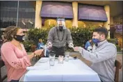  ?? Mel Melcon Los Angeles Times ?? JASON RUCKART, a managing partner at Roy’s in Woodland Hills, hands chopsticks to Nicole and Kyle Lehning as they dine alfresco in July.