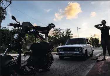  ?? ?? A dog stands on an electric motorcycle July 15 as people work on their electric motorcycle­s in Cojimar, Cuba.