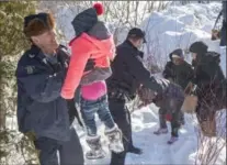  ?? PAUL CHIASSON, THE CANADIAN PRESS FILE PHOTO ?? Family members are helped into Canada by RCMP officers near Hemmingfor­d, Que., last year. Prime Minister Trudeau says a better economic future is not a reason to be granted refugee status.