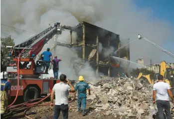  ?? KAREN MINASYAN/GETTY-AFP ?? Rescue workers comb the site of a retail market Sunday in Yerevan, the Armenian capital, after an explosion in a fireworks storage area sparked a fire, killing two people and injuring 60. Workers and volunteers searched amid still-exploding fireworks for victims who might have been trapped as firefighte­rs worked into the night to put out the blaze.