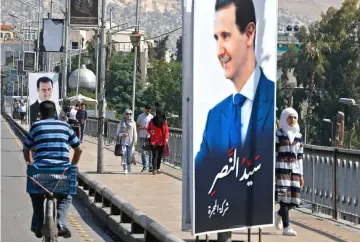  ??  ?? People walk near a portrait of Assad hanging in a street in Damascus. — AFP photo