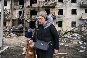  ?? Daniel Leal / Getty Images ?? A woman with a child walks in front of a damaged residentia­l building at Koshytsa Street, a suburb of the Ukrainian capital Kyiv, where a military shell allegedly hit on Friday.