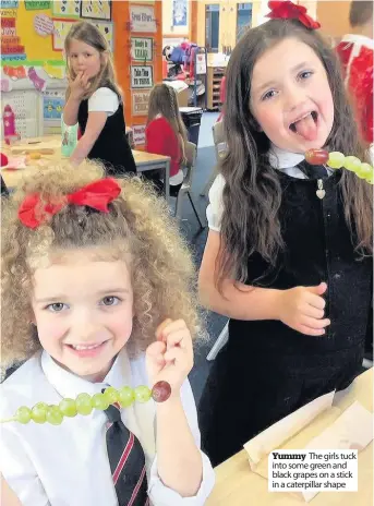  ??  ?? Yummy The girls tuck into some green and black grapes on a stick in a caterpilla­r shape