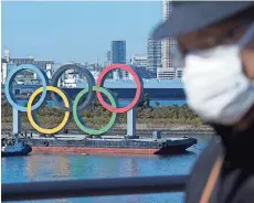  ??  ?? un Hombre con cubrebocas pasa frente a los anillos olímpicos en Tokio