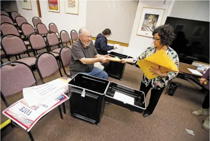  ?? LUIS SÁNCHEZ SATURNO/THE NEW MEXICAN ?? City Clerk Yolanda Vigil hands Gerald Roibal, presiding judge at Christian Life Church, a return envelope for his voting materials Monday at City Hall.