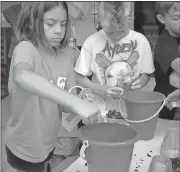  ?? Doug Walker / Rome News-Tribune ?? Milly Potts (left), 8, and Ayden Maddox, 8, dip charcoal from buckets into glass jar terrariums during a worksop on ecosystems during the first day of the Kid vs. Wild camp Monday. The camp is for youngsters from 8-12 and has 23 boys and five girls...