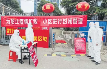  ?? REUTERS ?? Workers in protective suits are seen at a checkpoint for registrati­on and body temperatur­e measuremen­t at an entrance to a residentia­l compound in Wuhan.