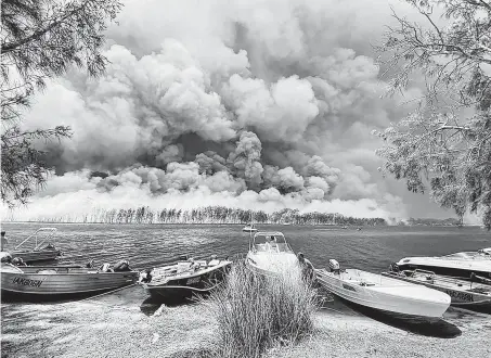  ?? Robert Oerlemans / Associated Press ?? Boats are pulled ashore as smoke and wildfires rage near Lake Conjola, Australia, as thousands of tourists flee.