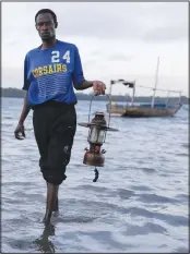  ?? ?? A fisherman comes out of the sea holding his hurricane lantern June 11 after a long night of fishing in the Shimoni Fishers Jetty in Kwale County, Kenya.