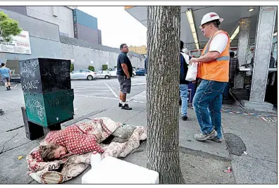  ?? AP ?? A man sleeps on the sidewalk as people line up to buy lunch at a Dick’s Drive-In in Seattle in May. The Seattle City Council has repealed a month-old tax on large employers that was intended to fund programs for the homeless.