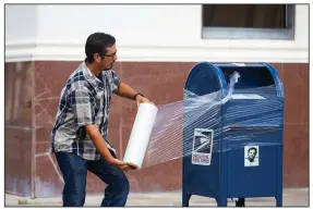  ?? (AP/Houston Chronicle/Mark Mulligan) ?? A U.S. Postal Service employee covers a mailbox with plastic wrap Tuesday in Galveston, Texas, to prepare for Hurricane Laura. More photos at arkansason­line.com/826laura/.