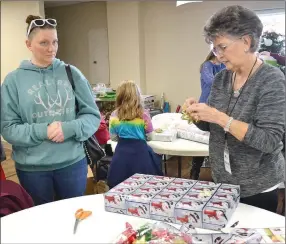  ?? TIMES photograph­s by Annette Beard ?? Linda Poe watches as Cinda Woolridge wraps the gifts she selected for her children. Hundreds of children will have Christmas gifts and dinner they would not have otherwise had thanks to the generosity of members of The Ridge Church and donors. Gifts were distribute­d Saturday, Dec. 17. For more photograph­s, go to the PRT gallery at https://tnebc.nwaonline.com/photos/.