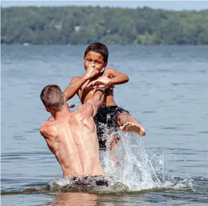  ?? Russ Dillingham/Sun Journal via AP ?? ■ Patrick Davis of Sabattus, Maine, heaves his stepson, Nikolas Jewette, into Sabattus Pond on Wednesday in Sabattus. Davis and his family visited the water to cool off on one of the hottest days of the year.