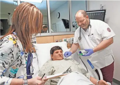  ?? ANGELA PETERSON / MILWAUKEE JOURNAL SENTINEL ?? Gateway Technical College Dean of Nursing Vicki Hulback (left) observes nursing student Brian Smith take the temperatur­e of Apollo, a patient simulator that talks, has a heartbeat and a pulse, and opens and closes his eyes.