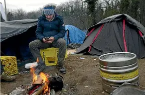  ??  ?? Ahmed, a Christian from Iran, checks his phone at a migrant camp in Calais for word on when he and his family might be able to make another attempt to cross the channel. The first one failed when their flimsy rubber boat threatened to sink.