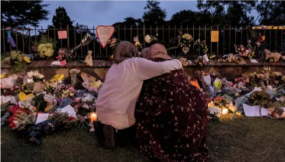  ??  ?? Mourners comfort each other amid the flowers, candles and mementoes brought by New Zealanders to a makeshi  memorial for the victims
