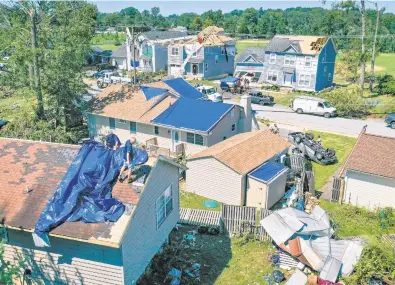  ?? JERRY JACKSON/BALTIMORE SUN PHOTOS ?? Austin Dodson, left, and Artie Hendricks, with Landmark Roofing, spread a tarp on a clients house in Londontown­e a day after a tornado tore through the area.