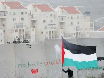  ?? MAJDI MOHAMMED/THE ASSOCIATED PRESS ?? The West Bank Jewish settlement of Modiin Illit is seen in the background while a protester waves a Palestinia­n flag in front of Israeli troops. The United Nations’ first report on the broad policy of Israeli settlement­s concluded Thursday.