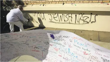  ?? Michael Macor / The Chronicle ?? An Oakland city worker paints over the anti-Semitic scrawl that was sprayed on Temple Sinai in Oakland.