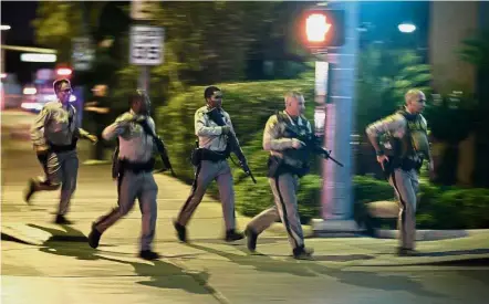  ??  ?? Getting into position: Police running to cover the scene of the shooting near the Mandalay Bay Resort and Casino on the Las Vegas Strip. — AP