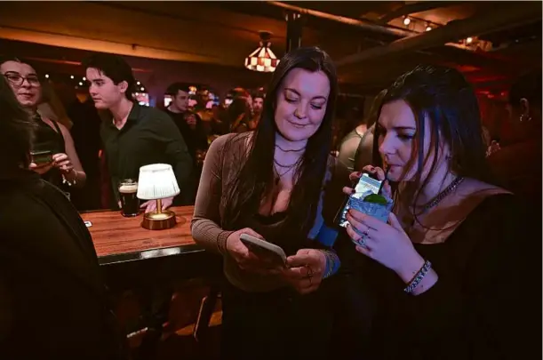  ?? PHOTOS BY JOSH REYNOLDS FOR THE BOSTON GLOBE ?? Sisters Sydney and Maggie Scanlon browsed Lola during a launch party for the dating app at Capo in South Boston. Lola is one of a trio of Boston-based apps attempting to challenge establishe­d apps Hinge, Bumble, and Tinder.
