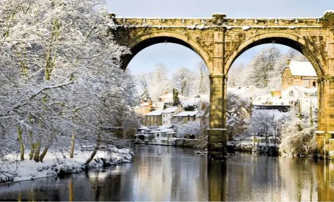  ??  ?? The magnificen­t castellate­d viaduct frames views of the town nestling at the edge of the calm River Nidd, overhung by bare branches marked in snow.