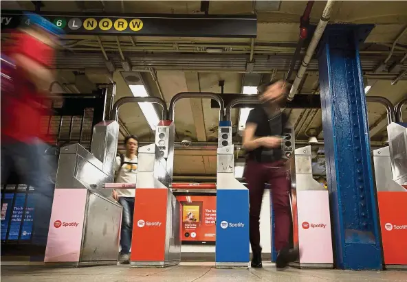  ??  ?? New advertiser­s: Commuters exit turnstiles displaying Spotify advertisem­ents at the Union Square subway station in New York. Upstarts have helped push up the price of certain subway campaigns in the past five years. — Bloomberg