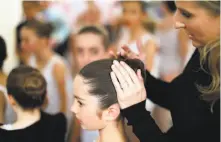  ??  ?? Ballet school teacher Kristi Decaminada checks a student's hair backstage before her performanc­e in the showcase.