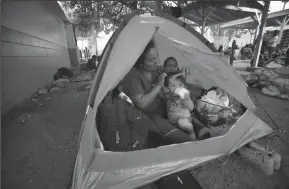  ?? NELVIN C. CEPEDA/SAN DIEGO UNION-TRIBUNE ?? Sitting in their tent, Ana Marlene Bueso combs the hair of her son David Pineda with her daughter Angela in the background. The family set up for the night at the temporary shelter at the Unidad Deportiva Benito Juarez, a municipal gym in Tijuana.