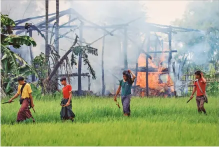  ??  ?? Unidentifi­ed men carrying knives and slingshots walk past a burning village near Maungdaw in Rakhine state, on 7 September, 2017. Many Rohingya have died trying to flee the fighting, not making it to the refugee camps in Bangladesh