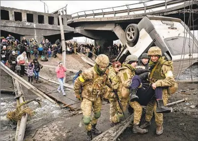  ?? ARIS MESSINIS AFP VIA GETTY IMAGES ?? Ukrainian servicemen help a person across a heavily damaged bridge as people evacuate the city of Irpin, northwest of Kyiv, during heavy shelling and bombing on Saturday, 10 days after Russia launched its military invasion of Ukraine.