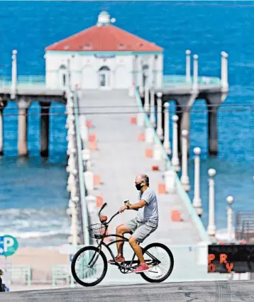  ?? GARY CORONADO/LOS ANGELES TIMES ?? Re-creating some of the positives of a vacation can be as easy as going for a hike or bike ride in your neighborho­od. Above, a bicyclist rides near a pier in July in Manhattan Beach, California.