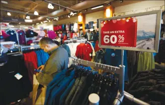  ?? Associated Press photo ?? In this 2018 photo, a last-minute shopper scans his mobile device next to a sign marking discounts on coats at a Columbia store as shoppers finish up their Christmas gift lists at the Outlet Malls in Castle Rock, Colo.