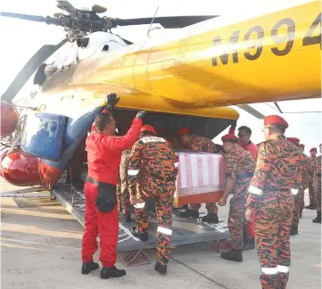  ??  ?? Firemen transfer the casket into a helicopter to be taken to Kampung Tian.