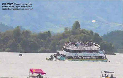  ??  ?? MAROONED: Passengers wait for rescue on the upper decks after a cruise boat capsized in a reservoir