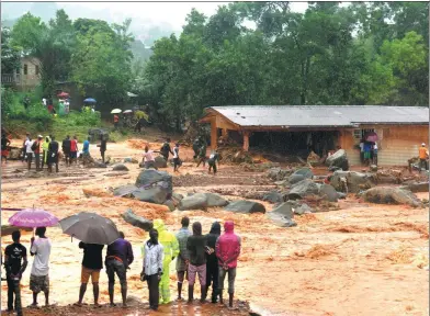  ?? SAIDU BAH / AGENCE FRANCE-PRESSE ?? Bystanders look on as floodwater­s rage past a damaged building in an area of Freetown on Monday, after three days of torrential rain struck the capital of the west African state of Sierra Leone.