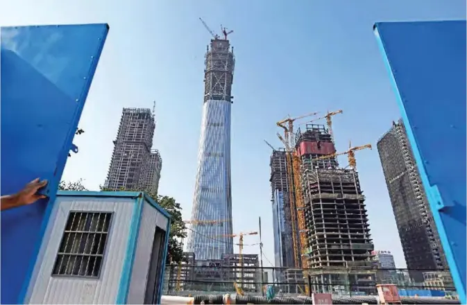  ?? — AFP ?? BEIJING: This picture taken on May 25, 2017 shows a guard closing a gate to a constructi­on project in Beijing’s central business district, as China Zun (2nd L), the city’s tallest building, is seen in the background.