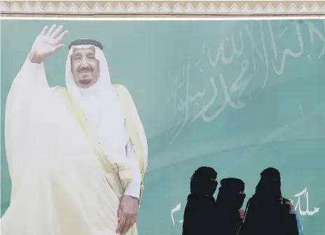  ?? Reuters ?? Women in Riyadh wearing the abaya and niqab walk past a poster of Saudi Arabia’s King Salman bin Abdulaziz