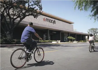  ?? Chris Carlson / Associated Press ?? Bicyclists pass in front of a closed Macy’s department store in Santa Ana in March. The retailer warned Thursday that it could lose more than $1 billion during its first quarter.