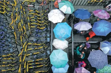  ?? HAO YI / FOR CHINA DAILY ?? People take cover from the rain as they wait at the Bawangfen bus station in Beijing on Friday, their umbrellas providing a contrast to the colorful bikes for hire.