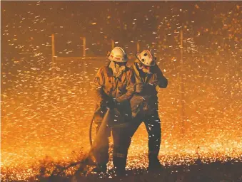  ?? SAEED KHAN/AFP VIA GETTY IMAGES ?? Firefighte­rs in Nowra, NSW, struggle in strong winds while trying to secure nearby houses. Ten more Albertan firefighte­rs have arrived to help as intense bushfires sweep Australia.