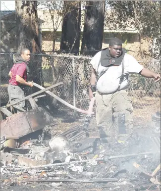  ?? Brodie Johnson • Times-Herald ?? The Forrest City Fire Department responded to a fire on Patillo Road in Forrest City Thursday that firemen said was caused by illegal and inattentiv­e burning of materials. FCFD Captain Chris Ray, left, helps firefighte­r Demarcus Hunter maneuver the water line through the debris as he moves in further to continue saturating the rubble.