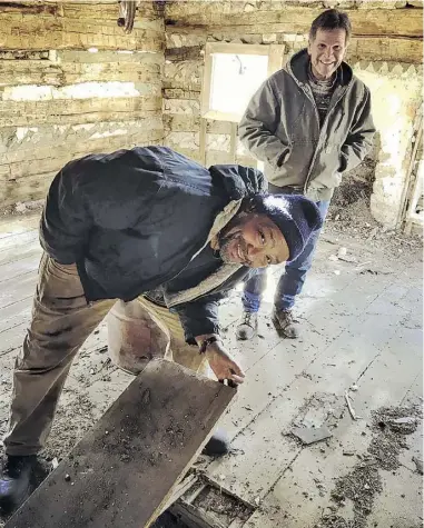  ?? BY JOHN MCCASLIN ?? Nils Aylor shows how ‘Dr. Crop’ would lift a floorboard of his rented cabin and produce a gallon of illicit whiskey. Behind Aylor is Mark Siess, who recently purchased the cabin for relocation to Madison County.