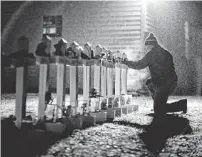  ?? AP ?? Frank Kulick adjusts a display on his lawn in Newtown, Conn., memorializ­ing the victims of the Sandy Hook Elementary shooting.