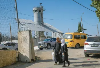  ?? MAHMOUD ILLEAN/AP ?? Palestinia­ns pass an Israeli military guard tower that has two robotic guns and surveillan­ce cameras on Oct. 6 at the Al-Aroub refugee camp. The robotic weapons can fire tear gas, stun grenades and sponge-tipped bullets.