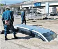  ??  ?? Police inspect a car buried in mud in Kure, Hiroshima prefecture, yesterday