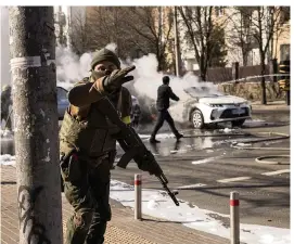  ?? EMILIO MORENATTI AP ?? Ukrainian soldiers take positions outside a military facility as two cars burn Saturday in a street in Kyiv, Ukraine.